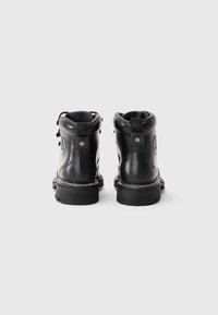 Par de botas de tornozelo de couro preto com solas grossas, alças traseiras e logótipos em relevo nas laterais, sobre um fundo branco liso.