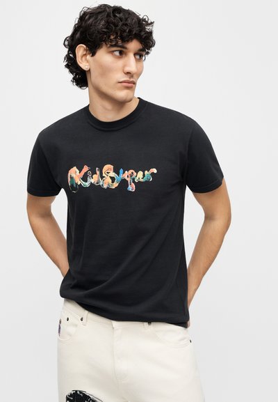Μαύρο βαμβακερό t-shirt με πολύχρωμο, καλλιτεχνικό λογότυπο "KidSuper". Μανίκια κοντά και κλασικός στρογγυλός λαιμός.