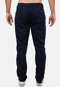Pantaloni blu navy con design a gamba dritta, con accenti di cucitura rossa, passanti per cintura e due tasche posteriori. Indossati con sneakers bianche.
