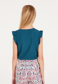 Top senza maniche a coste in verde acqua con dettagli a volant sulle spalle, abbinato a pantaloni multicolore con un design geometrico.