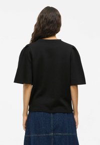 Črna majica s kratkimi rokavi in puffastimi rameni, izdelana iz gladkega materiala. Ima okroglo izreza in čist, minimalističen dizajn.