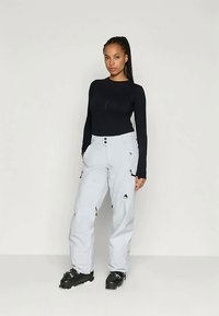 Calças de esqui cinza claro com bolsos funcionais e fechos, combinadas com uma t-shirt justa de manga longa preta. Apresenta uma textura suave e um design desportivo.