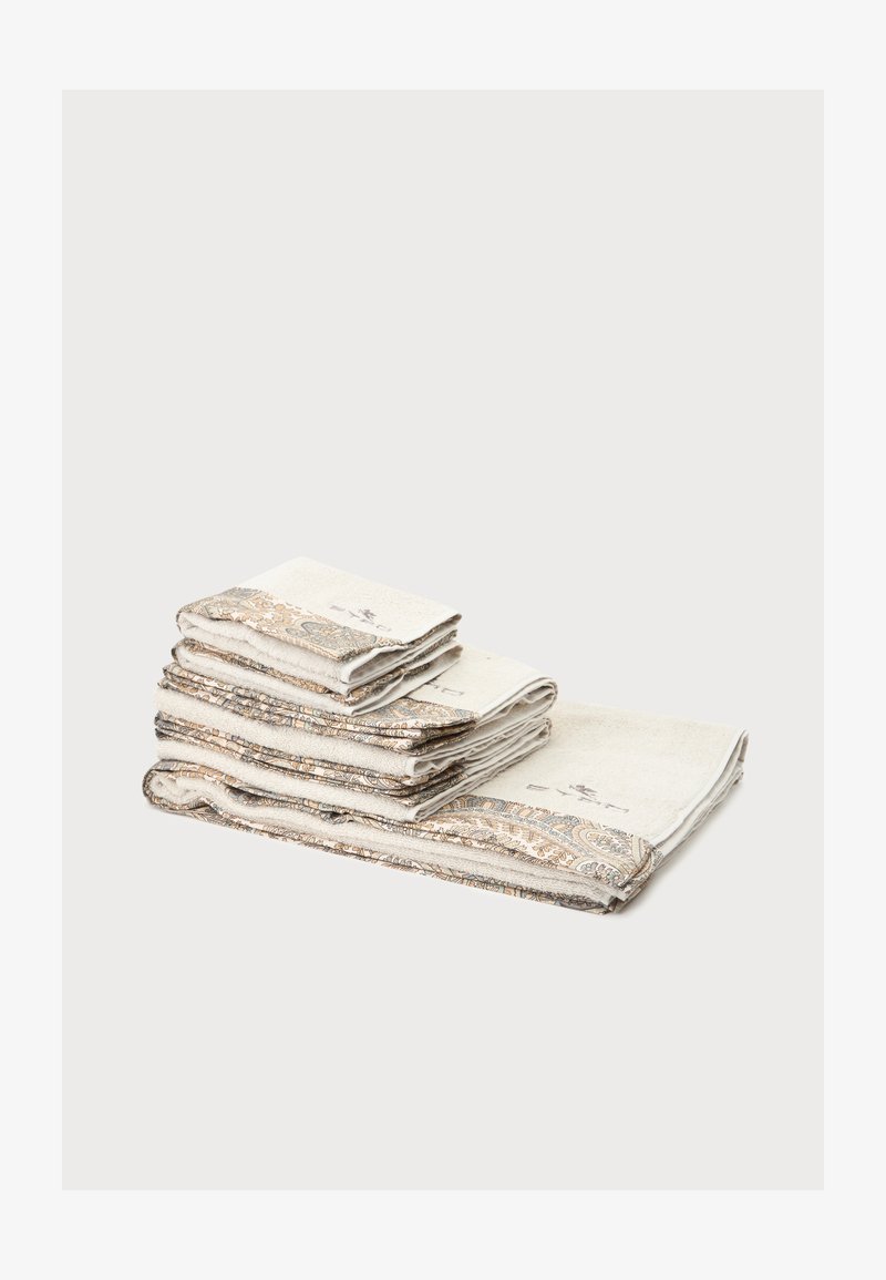 Pile de serviettes beige avec des bordures paisley dorées et bleues complexes, soigneusement pliées sur un fond blanc uni.