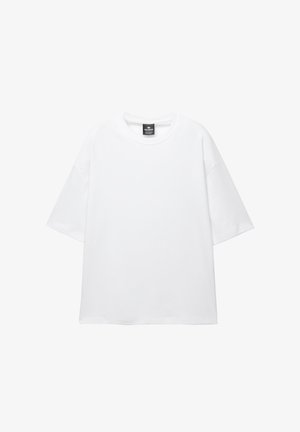 Witte oversized t-shirt met korte mouwen, ronde hals en zachte katoenen stof. Heeft een zwart label bij de hals. Geen patronen of accenten.