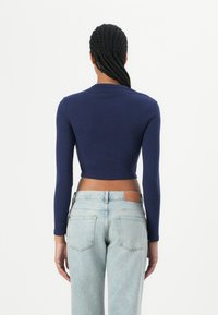 Navy fitted long-sleeve top with a round neckline, paired with high-waisted light blue jeans featuring a leather tag and classic pockets.