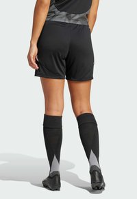 Șorturi negre de fotbal cu o textură netedă, asortate cu șosete negre și gri până la genunchi, cu un model în diamant, și ghete negre.