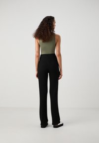 Tělové body olivově zelené barvy v přiléhavém střihu, kombinované s černými žebrovanými kalhotami s vysokým pasem. Textura tělového body je hladká, vzor kalhot je pruhovaný.