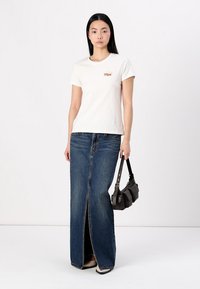 Vit bomullst-shirt med kort ärm och en liten grafik, kombinerad med en mörkblå denim-maxikjol med slits framtill, och en svart handväska.