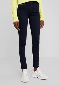 Jeans skinny azul oscuro hechos de denim, con un diseño clásico y acentos minimalistas. Combinados con zapatillas deportivas blancas.