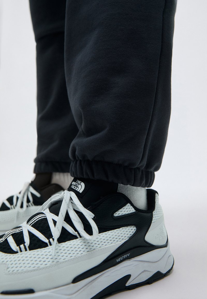 Sort joggers med elastiske manchetter, parret med sort og hvid sneakers med mesh-paneler, snørebånd og logo-detaljer.
