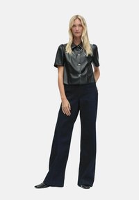 Czarna, sztuczna skórzana koszula z krótkim rękawem, okrągłym kołnierzykiem i srebrnymi guzikami, połączona z ciemnoniebieskimi spodniami o wysokim stanie i szerokich nogawkach.