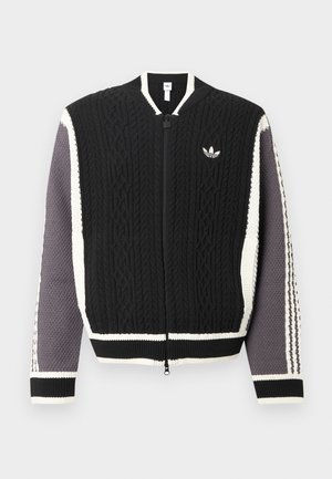 Pletena jakna z zadrgo spredaj v črni barvi z teksturiranimi vzorci, belimi poudarki in sivimi rokavi. Z ribanim robom in manšetami. Prisoten logotip Adidas.