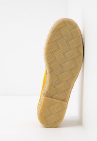 Semelle de chaussure espadrille jaune avec motif de bande de roulement en caoutchouc tissé, taille 37, reposant verticalement contre une surface blanche.