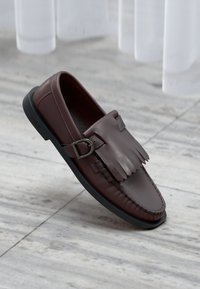 Mocassins en cuir marron avec un accent à franges et un détail de boucle. Présentent une semelle en caoutchouc noire et un design cousu le long des bords.