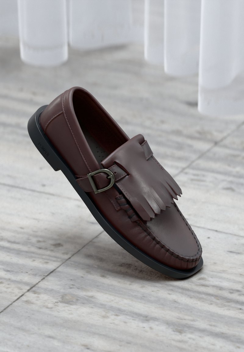 Barna bőr loafferek frufruval és csattal díszítve. Feketére festett gumi talppal és a széleken végigfutó varrással rendelkezik.