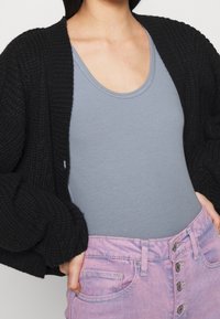 Svart stickad cardigan, ljusblå ribbad tanktop och rosa högmidjade jeanstights med knappstängning och framfickor.