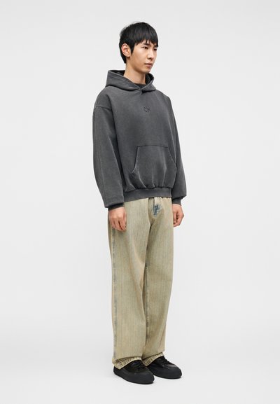 Γκρι φαρδιά φούτερ με μπροστινή τσέπη, συνδυασμένο με ανοιχτόχρωμο ριγέ τζιν παντελόνι και μαύρα αθλητικά παπούτσια. Λείο ύφασμα και χαλαρή εφαρμογή.