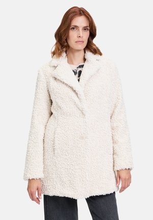 Cappotto bianco, testurizzato, realizzato in un tessuto morbido e peloso. Presenta un colletto a poncho, chiusura con bottoni e due tasche laterali. Vestibilità morbida.