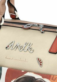 Sac à main en cuir beige présentant un logo argenté, des accents texturés, une fermeture éclair avec des charms décoratifs, et un panneau coloré à motifs en bas.
