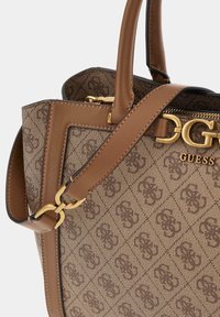 Sac à main marron de la marque Guess avec un tissu à motifs, des finitions en cuir, des accessoires en métal doré, des poignées doubles et une bandoulière ajustable.