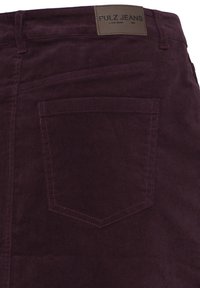 Poche arrière d’un pantalon en velours côtelé violet foncé avec une étiquette en cuir marron indiquant le nom de la marque Pulz Jeans.