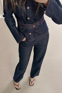 Temno modra jeans jakna in hlače s rdečimi šivi, ki vključujejo srebrne gumbe, pasom in sproščenim fitom.