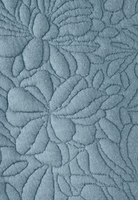 Tejido azul claro con un patrón floral en relieve que presenta hojas y pétalos texturizados, creando una superficie suave y táctil.