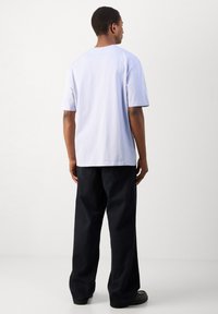 Fehér pamut rövid ujjú póló kerek nyakkivágással, fekete, bő szabású nadrággal és fekete cipővel párosítva. Egyszerű, hátulnézet.