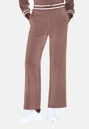 Brązowe szerokie spodnie dresowe z kieszeniami noszone z białymi tenisówkami oraz dopasowany brązowy top z białymi paskami na mankietach i talii.
