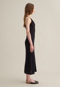 Abito lungo in maglia nera con spalline sottili, corpino aderente e orlo svasato. Abbinato a ballerine nere con punte appuntite e dettagli dorati.