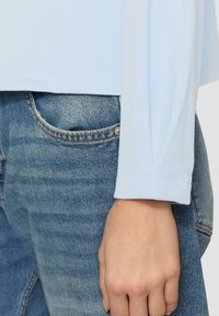 Lichtblauw langarmshirt met een zachte textuur, gecombineerd met lichtblauwe denim jeans, voorzien van een klassieke zak en subtiele stiksels.
