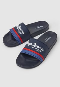Mornarske natikače z širokim trakom, na katerem je napis "Pepe Jeans" v beli barvi, z rdečimi in modrimi poudarki na teksturirani površini.