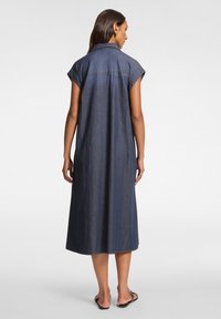Abito camicia in denim blu scuro, con maniche corte, colletto e una vestibilità ampia, che arriva fino a metà polpaccio, con dettagli minimi.