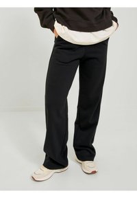 Black sweatpants made of soft fabric, featuring a relaxed fit, slightly flared legs, and side pockets, paired with light-colored sneakers.