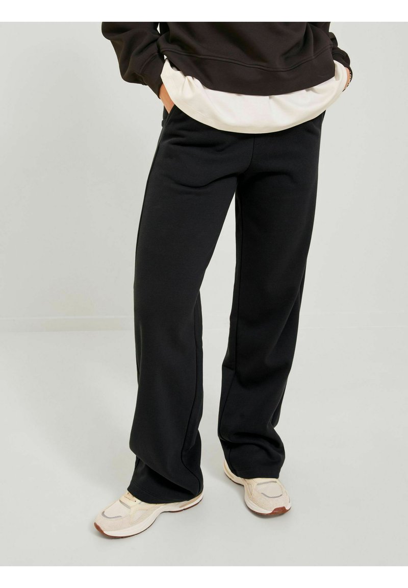 Black sweatpants made of soft fabric, featuring a relaxed fit, slightly flared legs, and side pockets, paired with light-colored sneakers.