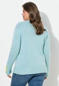 Světlomodrý pletený svetr s žebrovaným lemem a žlutým akcentem na rukávech, s volným střihem a texturovaným povrchem.