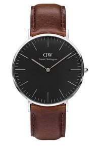 Cadran rond noir de montre Daniel Wellington avec des marqueurs d'heure et des aiguilles argentés, associé à un bracelet en cuir marron. Heure : 10h09.
