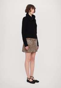 Svart stickad tröja med hög krage, tillsammans med en kjol i leopardmönster. Svarta balettinspirerade skor med dekorativa nitar fulländar outfiten.