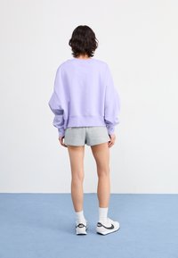 Lavender oversized sweatshirt made of soft fabric, paired with grey shorts. Features a round neckline and ribbed hem. White athletic shoes complete the look.