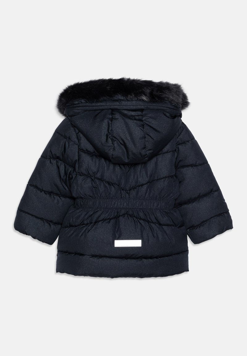 Veste matelassée navy avec capuche en fausse fourrure, taille cintrée et texture matelassée horizontale. Présente un patch logo réfléchissant au dos.