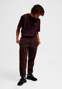 Bordeauxfarvet træningssæt med en løstsiddende t-shirt og bukser med snor, begge med logodetalje. Sorte sneakers fuldender looket.