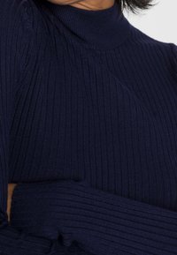 Granatowy sweter z golfem, wykonany z prążkowanej dzianiny, o dopasowanym kroju i długich rękawach. Dodatkowe cechy to wysoki golf i prążkowane mankiety.