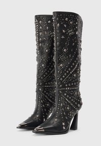 Par de botas de cuero negro hasta la mitad de la pantorrilla con puntas metálicas puntiagudas, tacones altos y complejas decoraciones de estrellas y tachuelas en plata.