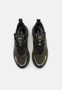 Schwarze und goldene Sport-Sneaker mit einem strukturierten Mesh-Obermaterial, gepolstertem Schaft und Logo-Akzenten. Sie verfügen über eine flexible Außensohle und kontrastierende Verzierungen.