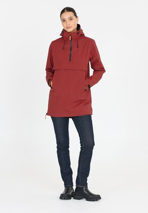 Red waterproof jacket with a front zipper, adjustable hood, and pockets, paired with dark jeans and black ankle boots. Simple design.