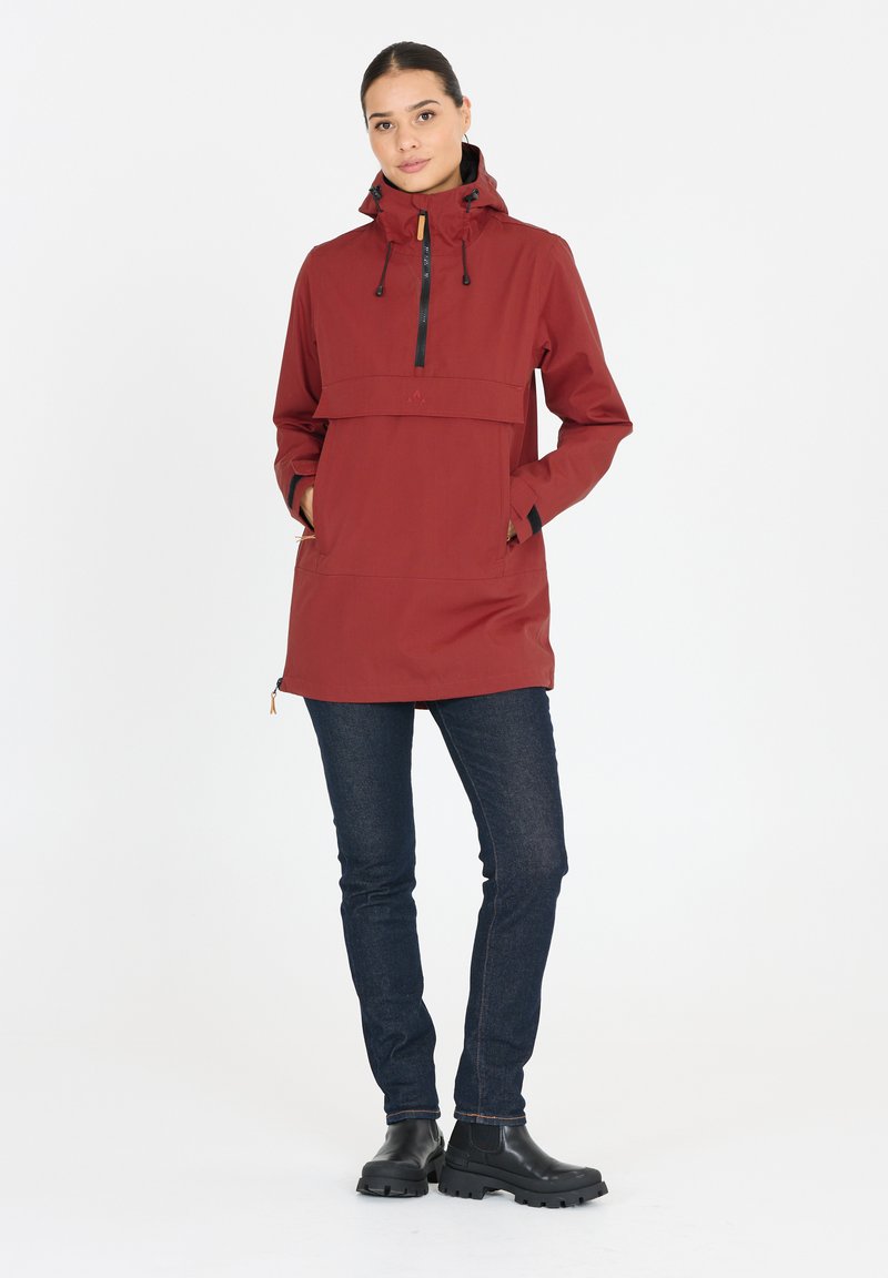 Röd vattentät jacka med frontdragkedja, justerbar huva och fickor, i kombination med mörka jeans och svarta ankelboots. Enkelt design.