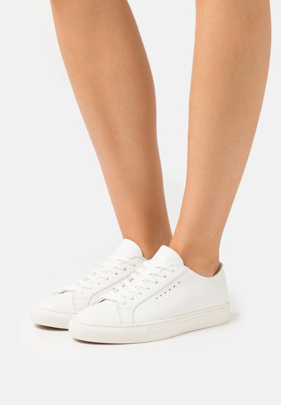 White leather sneakers with rounded toe, lace-up design, and small perforations on the sides. Solid rubber sole and minimalistic style.