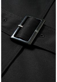 Zbliżenie czarnego pasku z materiału z prostokątną czarną metalową klamrą i widocznym przeszyciem na materiale.