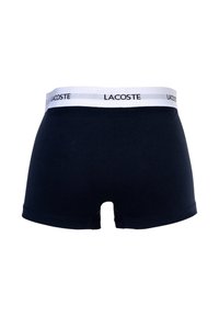 Marineblaue Boxershorts aus Baumwolle mit einem weißen Bund, der das Logo "LACOSTE" in Schwarz zeigt. Glatte Textur und eng anliegendes Design.