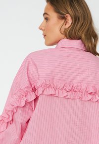 Red and white striped shirt featuring a ruffled accent along the back neckline. Made from a lightweight fabric with a smooth texture.